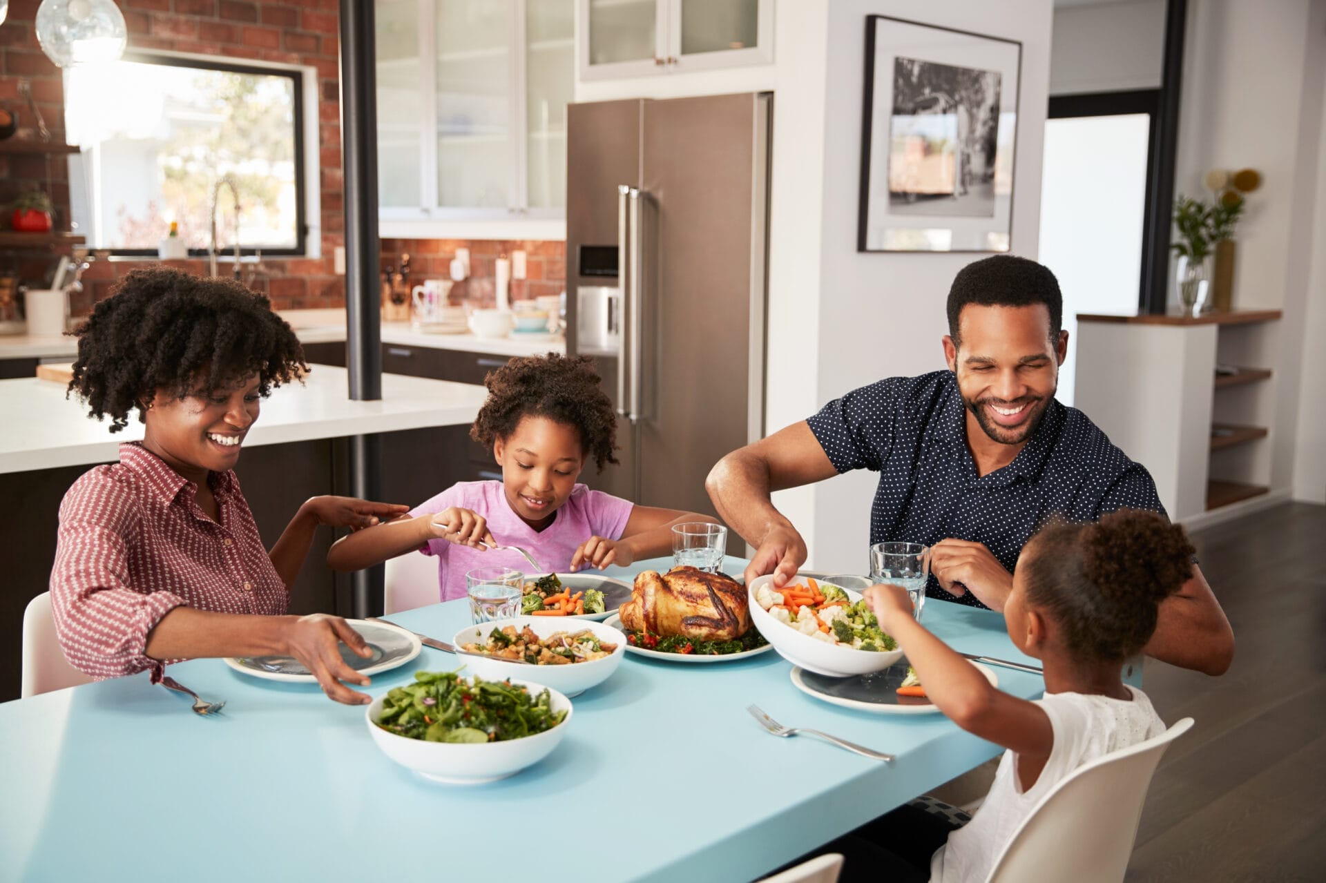A family smiling while eating at a table in the kitchen and enjoying their meal.